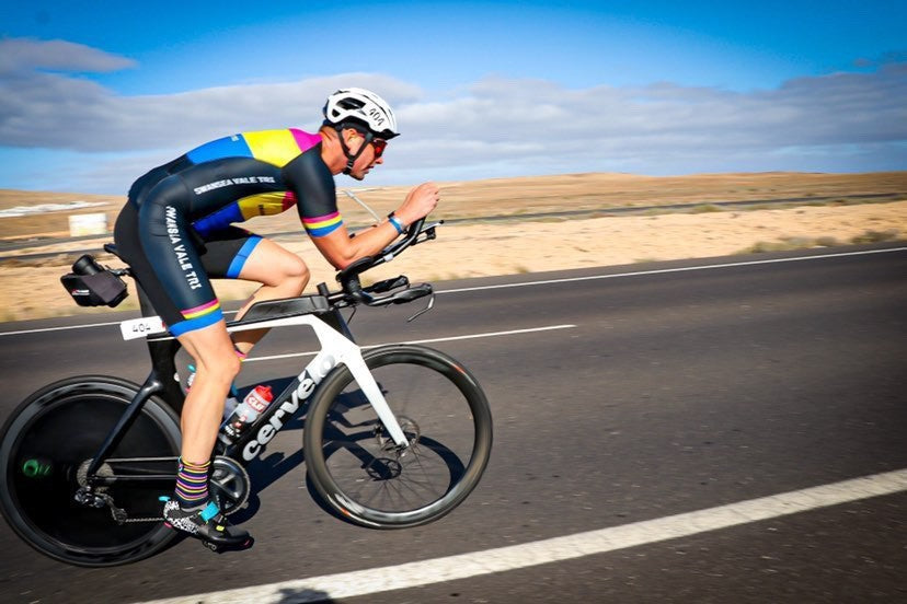 Triathlete riding a professional time trial bike on an open road during a race.