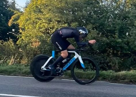 Triathlete riding a Giant aero bike with a disc wheel cover on a paved road.