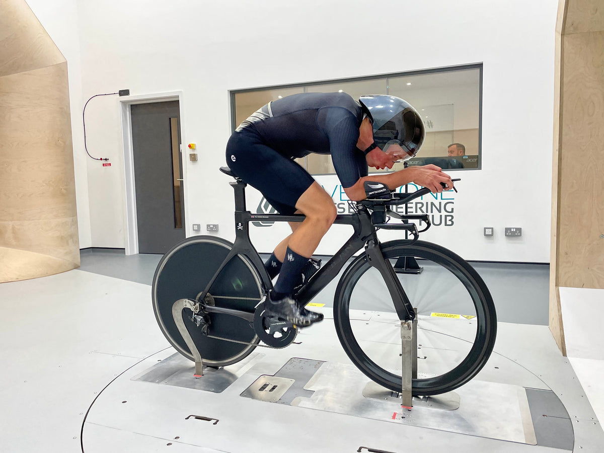 Triathlete in aerodynamic gear testing a disc wheel bike in a wind tunnel.