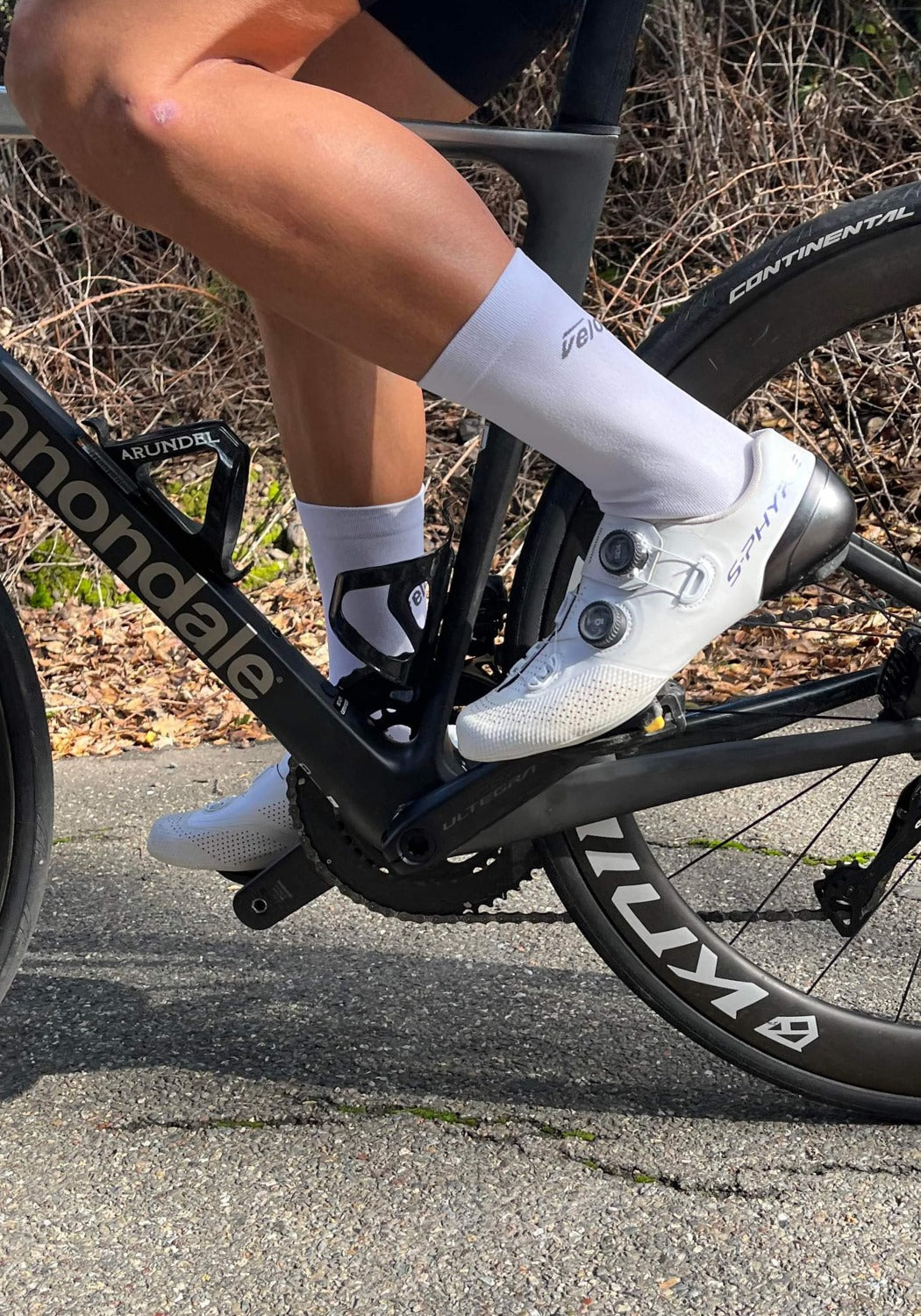Cyclist on road bike wearing white cycling shoes and veloToze socks