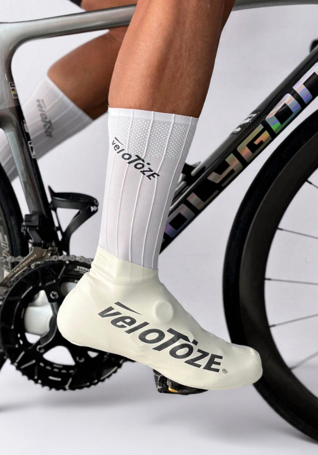 Cyclist wearing white veloToze shoe covers and socks on a road bike, close-up view