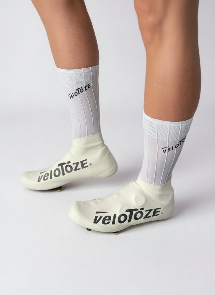 White cycling shoe covers and socks with veloToze logo on a cyclist's legs, studio background
