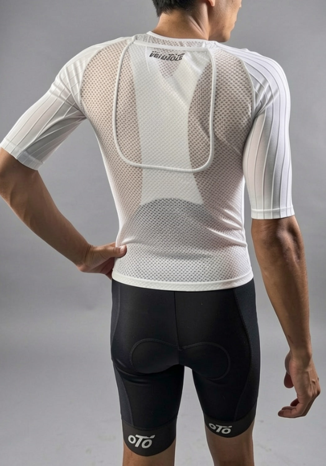 Cyclist wearing a white mesh short sleeve base layer and black cycling shorts, back view