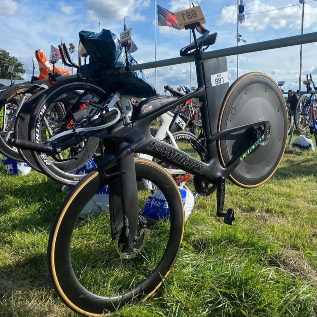 Black triathlon racing bike with aerodynamic disc wheel and carbon frame on a rack.