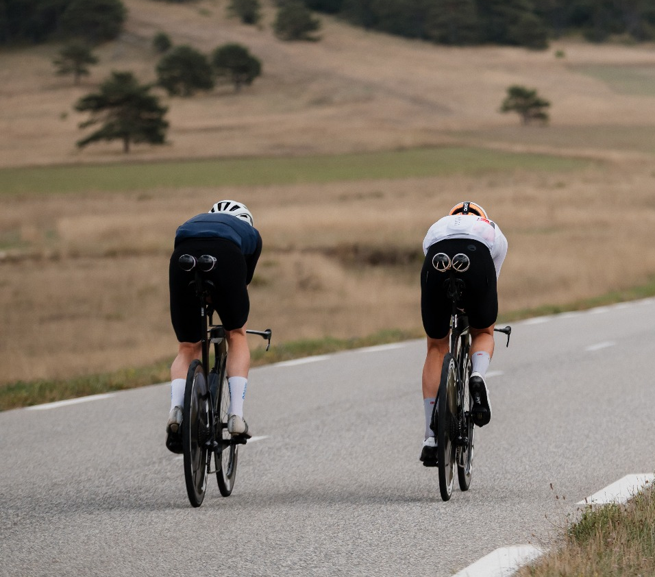 Two triathletes riding road bikes with disc wheel covers on an asphalt road.