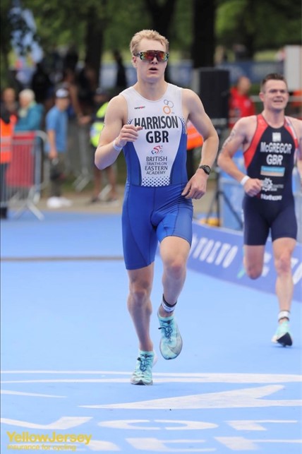 Male triathlete in blue racing kit running on a blue track during a competition.