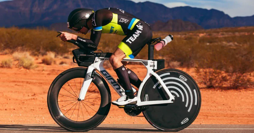 Triathlete riding a white Giant aero bike with disc wheel covers in a desert landscape.