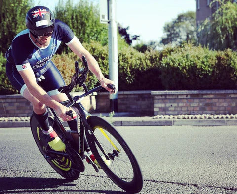 Triathlete in aero gear riding a racing bike on a sunny road.