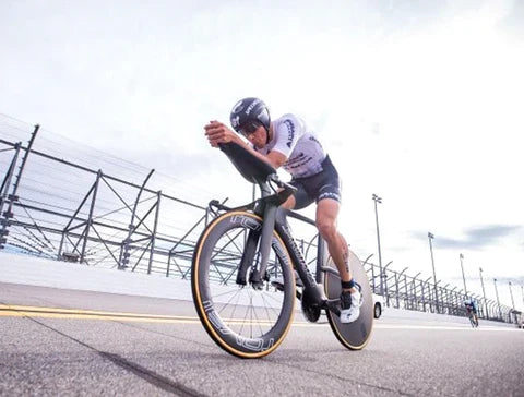 Triathlete riding a performance bike with aerodynamic disc wheels on an outdoor track.
