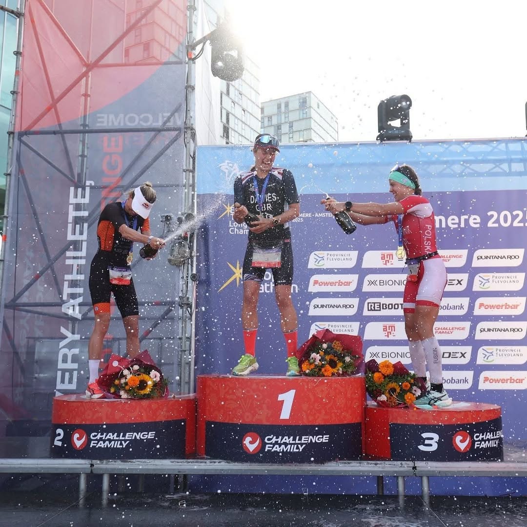 Triathlon podium winners celebrating with water spray at a Challenge Family event.