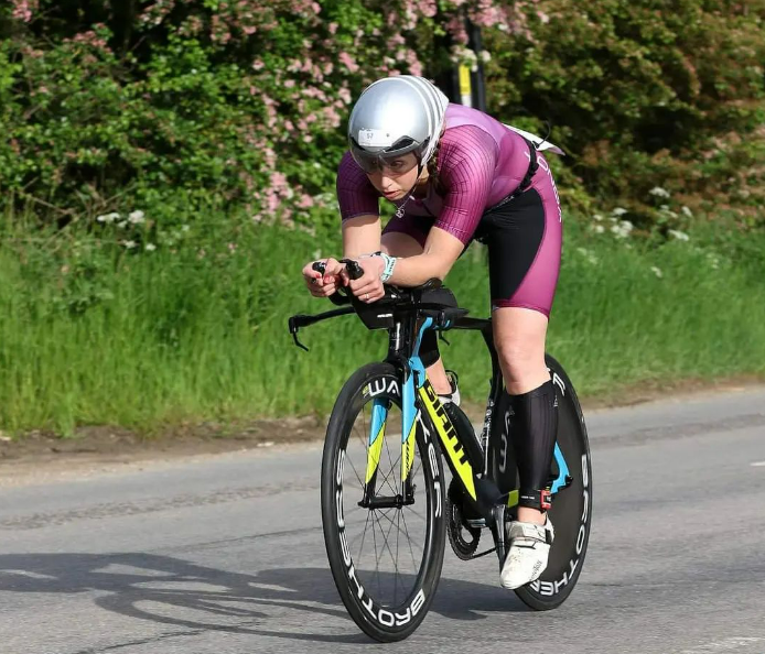 Triathlete in purple cycling kit riding a time trial bike with disc wheels on a road.