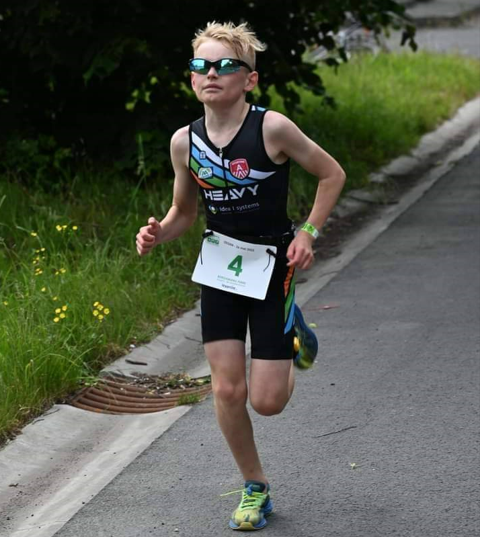 Young male athlete running in a triathlon race wearing a black singlet and sunglasses.