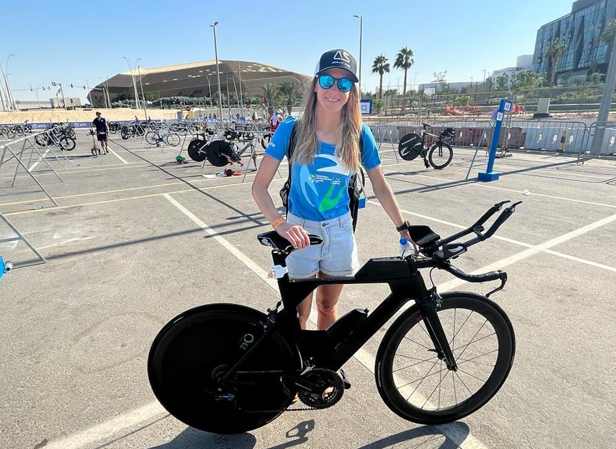 Female athlete posing with a triathlon bike featuring a rear disc wheel cover.