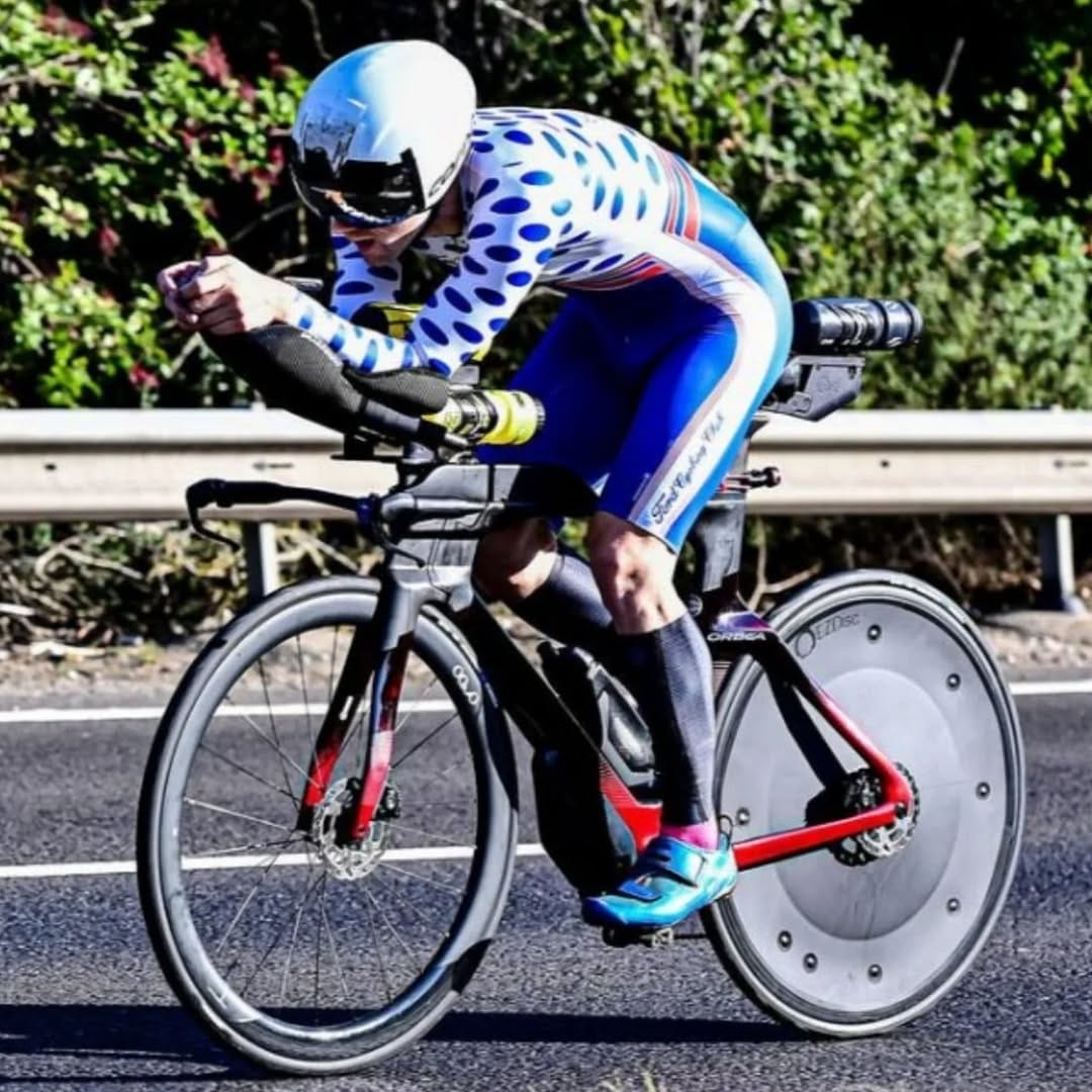 Triathlete riding a performance bike with a rear disc wheel cover on an asphalt road.