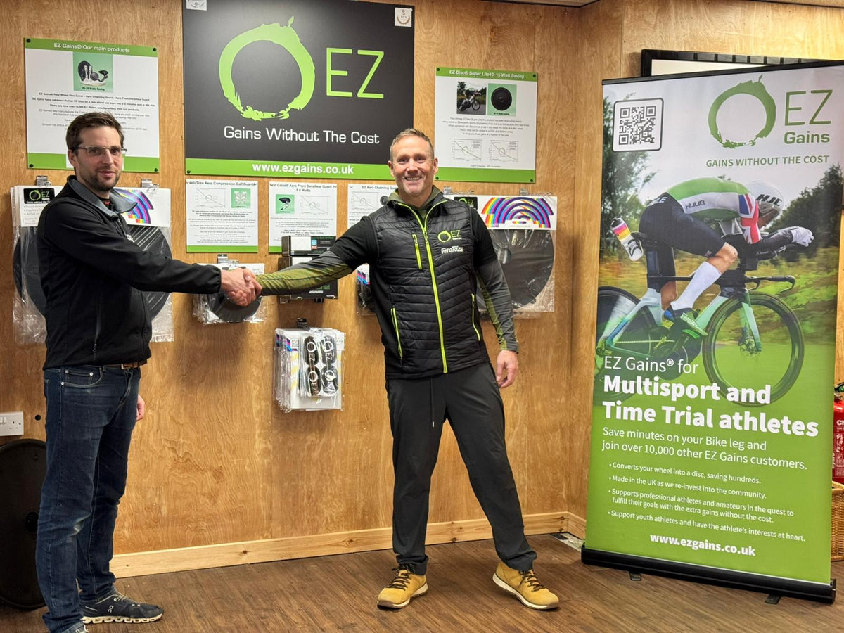 Two men shaking hands in a showroom featuring triathlon bike aerodynamic accessories.