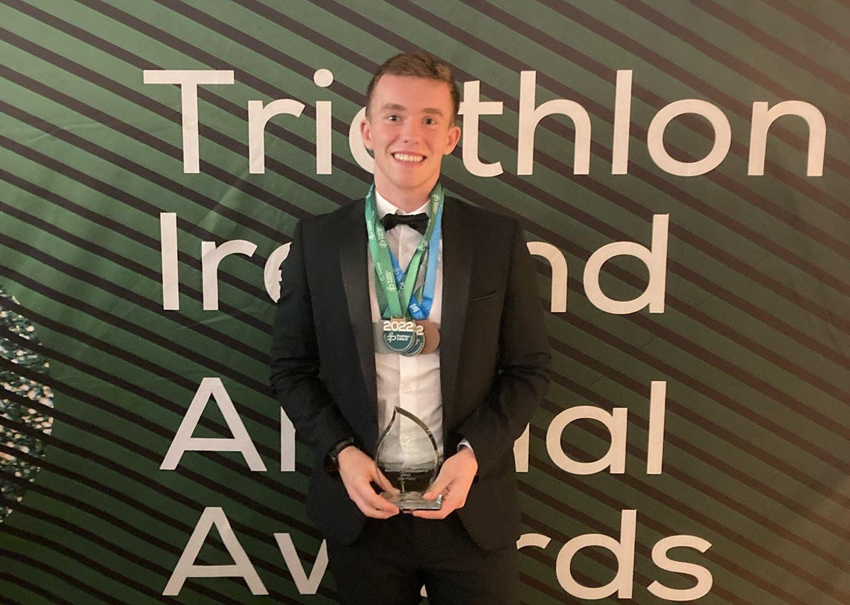 Smiling young man in a black suit and bowtie holding an award at the Triathlon Ireland Awards.