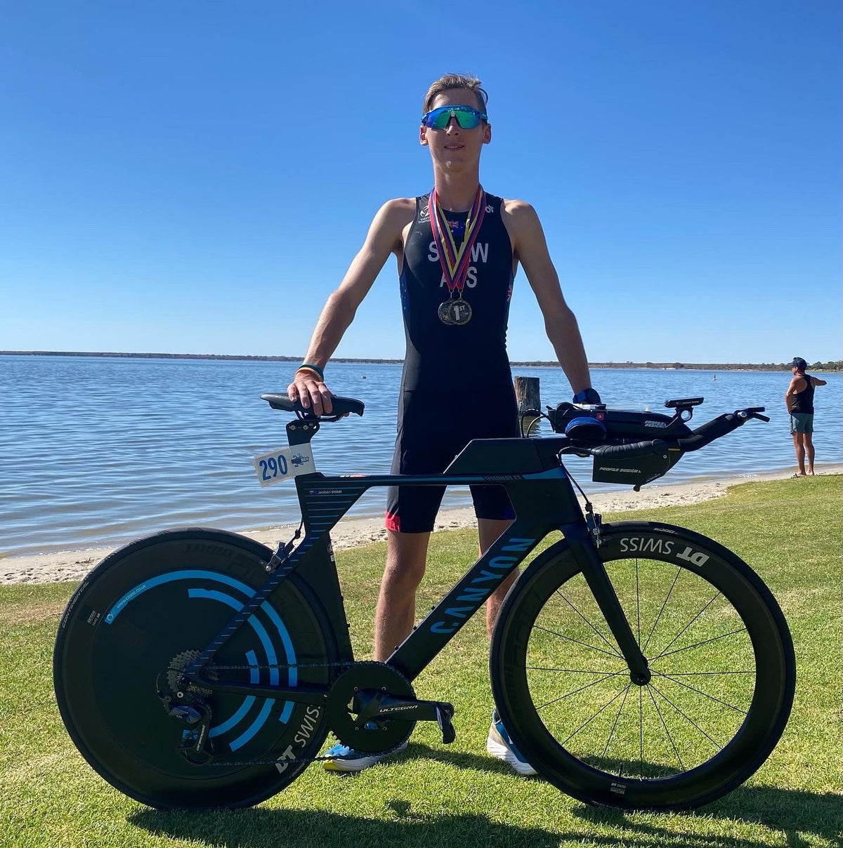 Triathlete with medal posing with a Canyon triathlon bike on grass by the ocean.