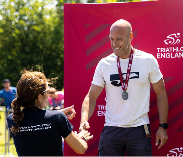 A smiling male athlete wearing a silver medal at a British Triathlon event.