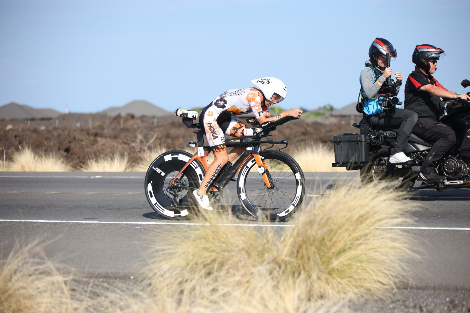 Triathlete riding an aerodynamic triathlon bike with a disc wheel on a paved road.
