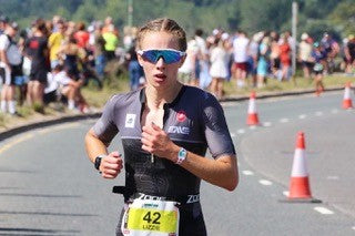 Female triathlete wearing sunglasses and race bib 42 running on a road course.