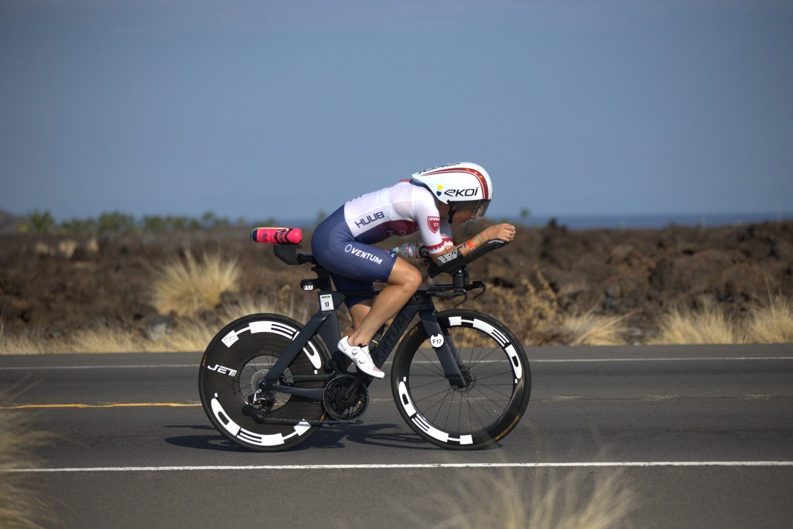 Triathlete riding a performance bicycle with aerodynamic disc wheel covers on a paved road.