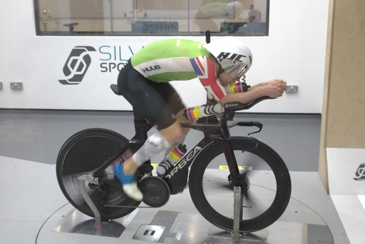 Triathlete in aerodynamic position testing a disc wheel bike on a wind tunnel platform.