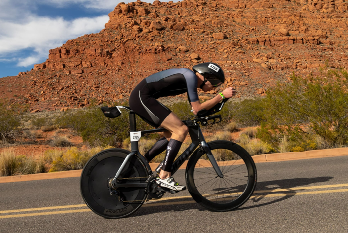 Triathlete riding a time trial bike with a disc wheel cover on a desert road.
