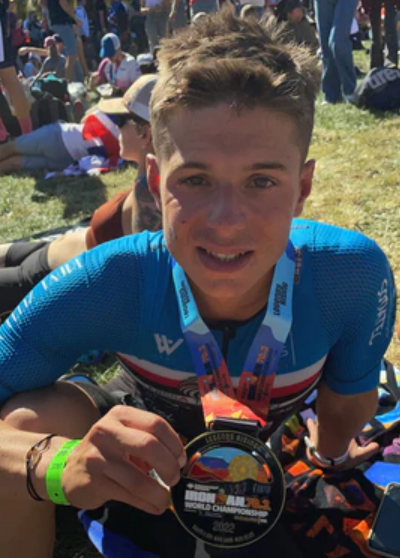Smiling male triathlete wearing a blue jersey and an Ironman 70.3 World Championship medal.