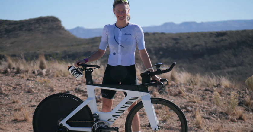 Female triathlete smiling with her white Canyon triathlon bike in a desert landscape.