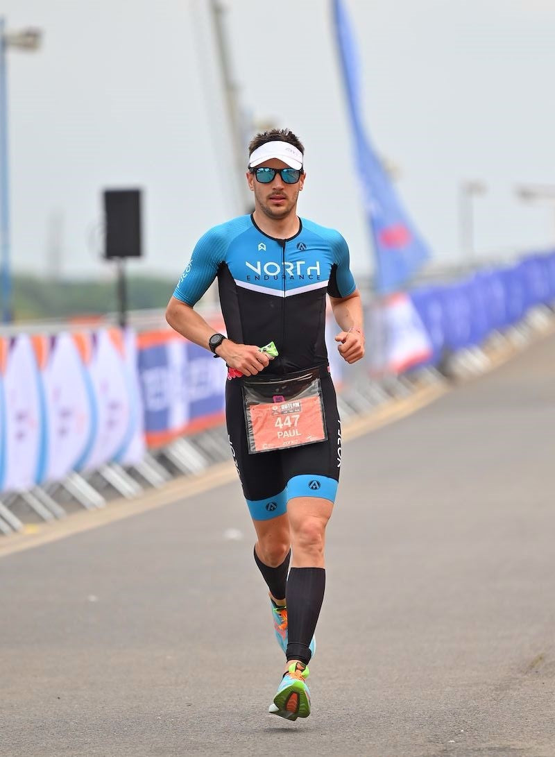 Male triathlete in blue racing kit running during a competition on an outdoor course.