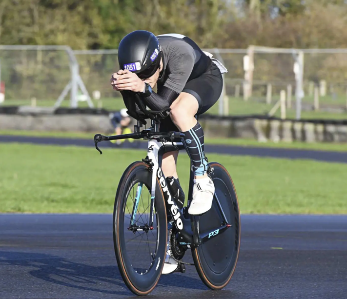 Triathlete riding a Cervelo P3 bike with a rear disc wheel cover on an asphalt track.