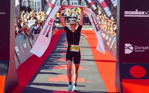 Female triathlete crossing the finish line at an Ironman 70.3 race event.
