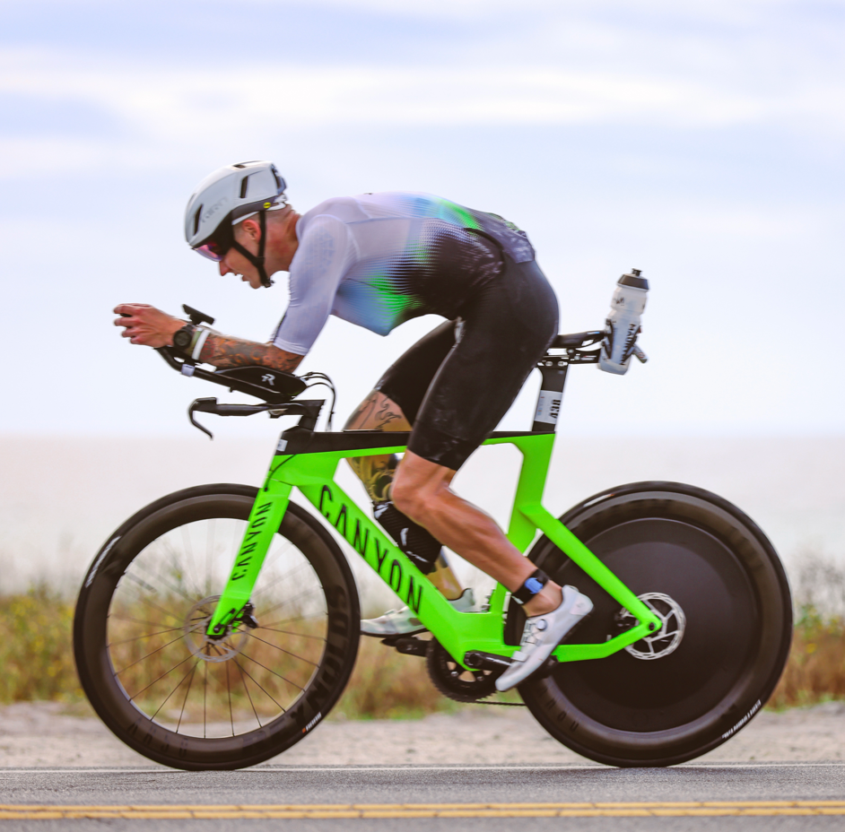 Ein Triathlet fährt auf einer Küstenstraße ein neongrünes Canyon-Aero-Rad mit Hinterradscheibenabdeckung.