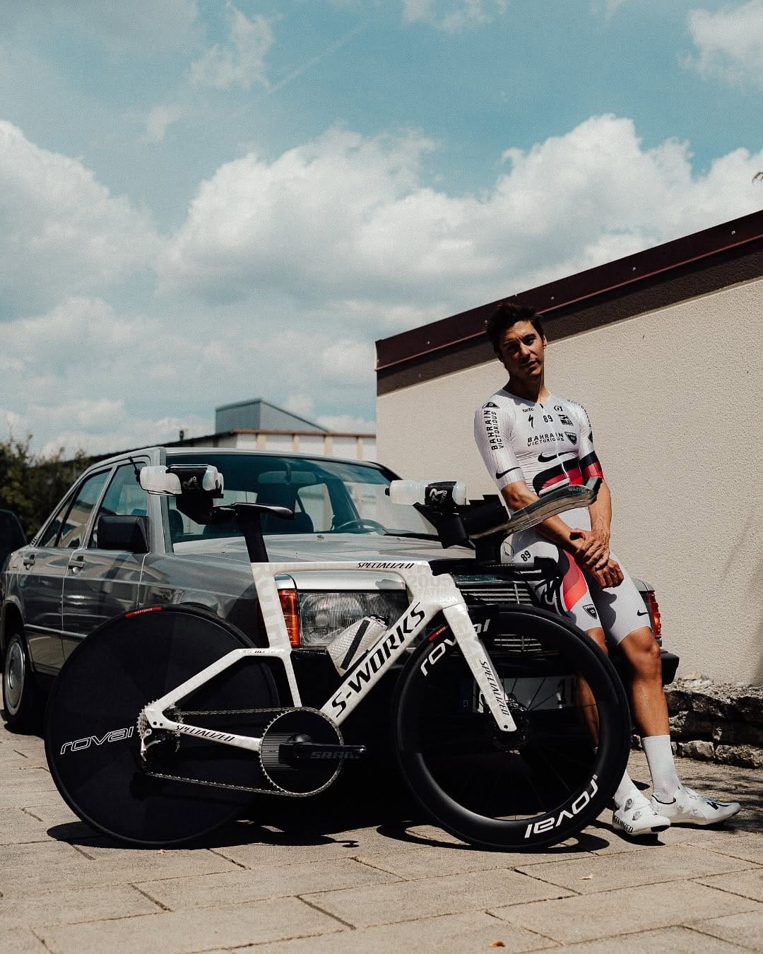 Triathlete posing with a white S-Works racing bike and a vintage car outdoors.