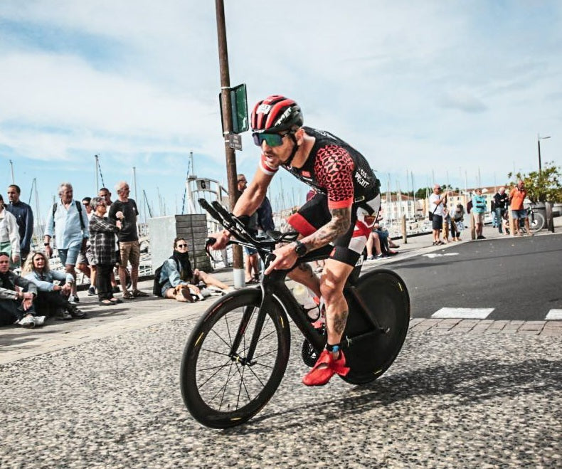 Triathlete riding a racing bike with a rear disc wheel cover on a paved road.