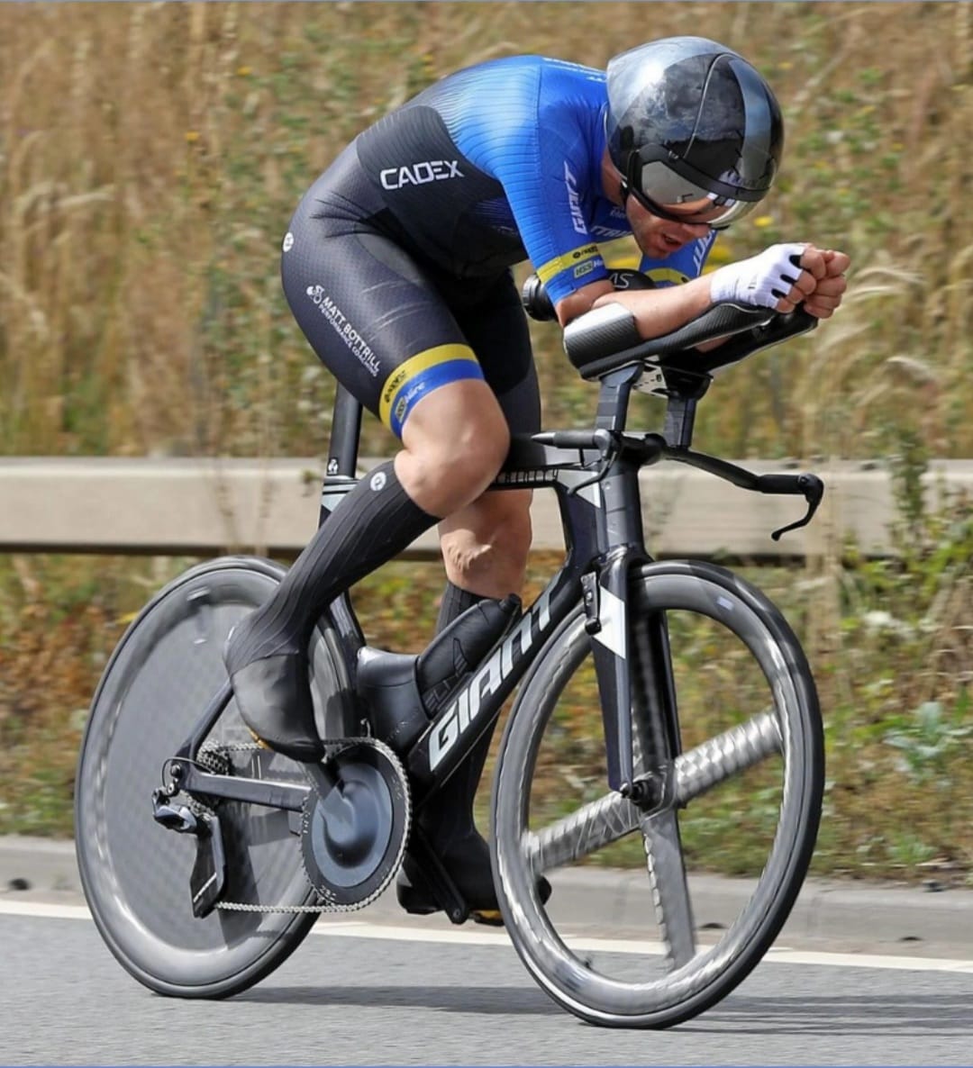 Triathlete riding a Giant aero bike with a disc wheel cover and chainring guard.