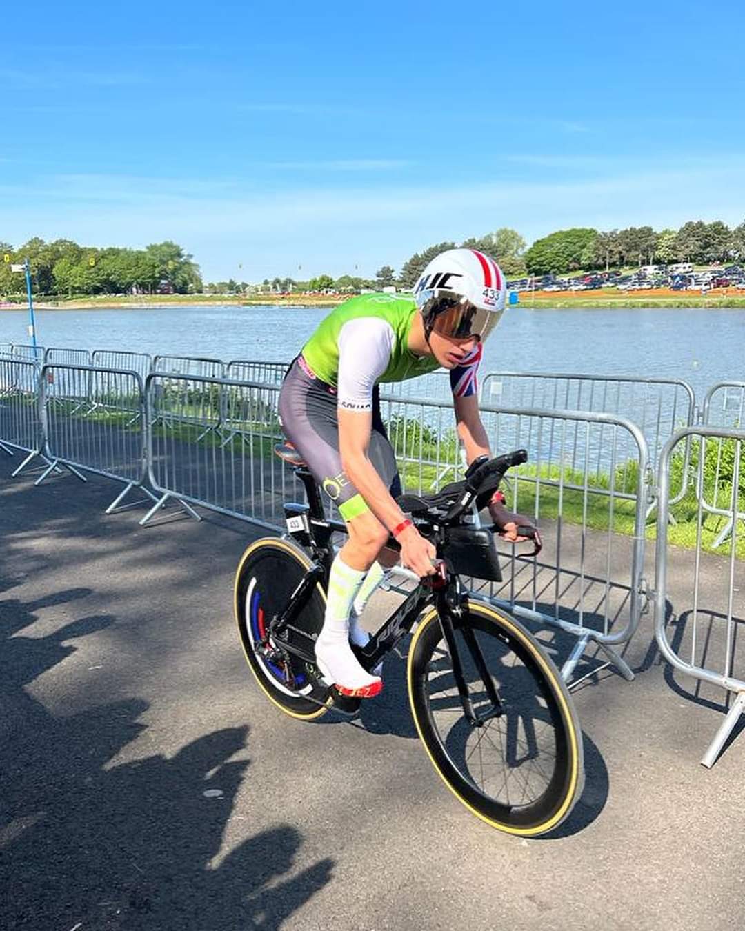 Triathlete riding a performance bike with aerodynamic disc wheel covers near a lake.