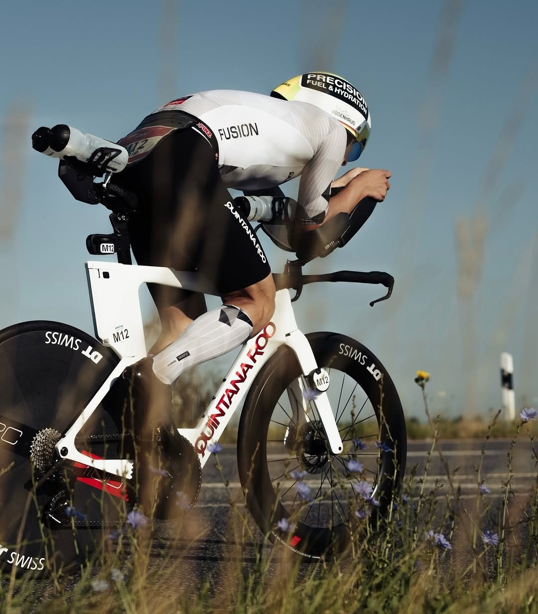 Triathlete riding a white Quintana Roo aero bike on an asphalt road.