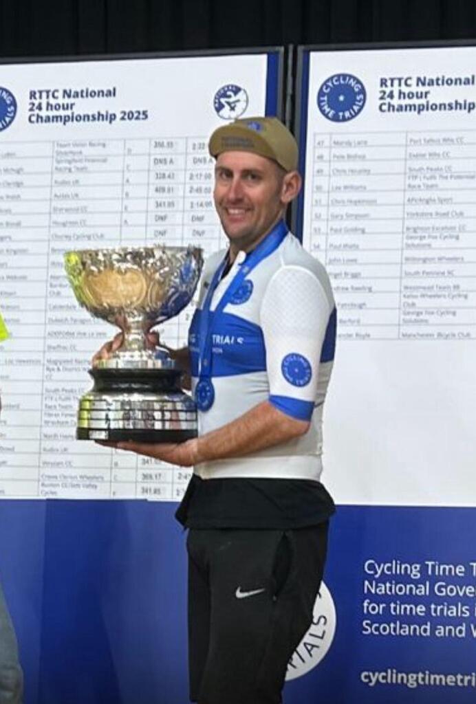 Male cyclist in white jersey holding a large silver trophy at a national championship event.