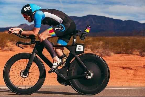 Triathlete riding a performance bike with aerodynamic disc wheel covers on a desert road.