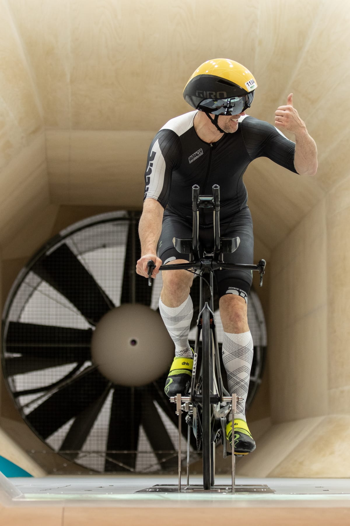 Triathlete in aerodynamic gear riding a stationary bike in a wind tunnel for testing.