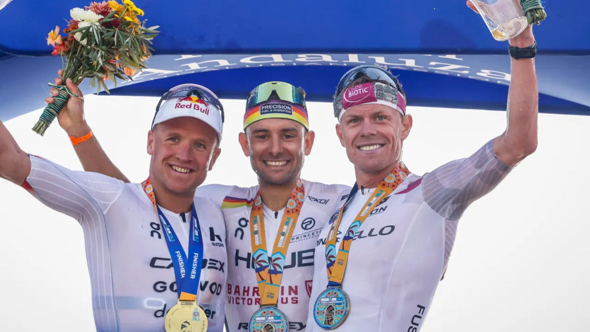 Three male triathletes celebrating on a podium wearing medals and cycling gear.