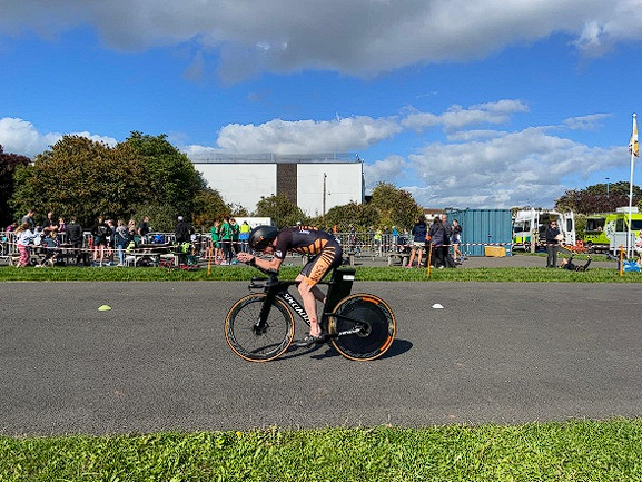 Triathlete riding a performance bike with a rear disc wheel cover on an asphalt track.