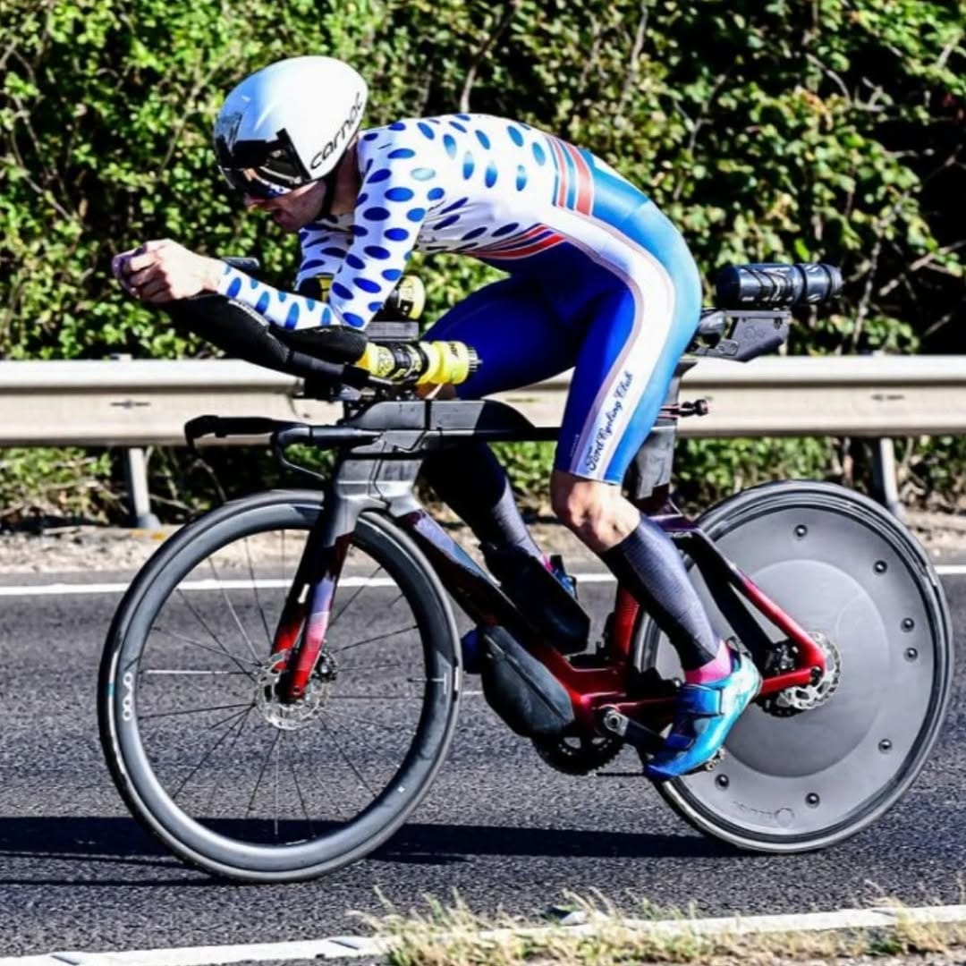 Cyclist in a racing suit riding a time trial bike on a road with greenery in the background
