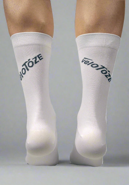 Person wearing white cycling socks with veloToze logo, back view on neutral background