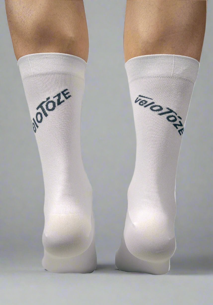 Person wearing white cycling socks with veloToze logo, back view on neutral background