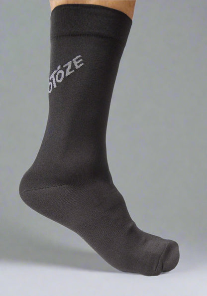 Black cycling sock with partial visible text, worn on foot, gray background