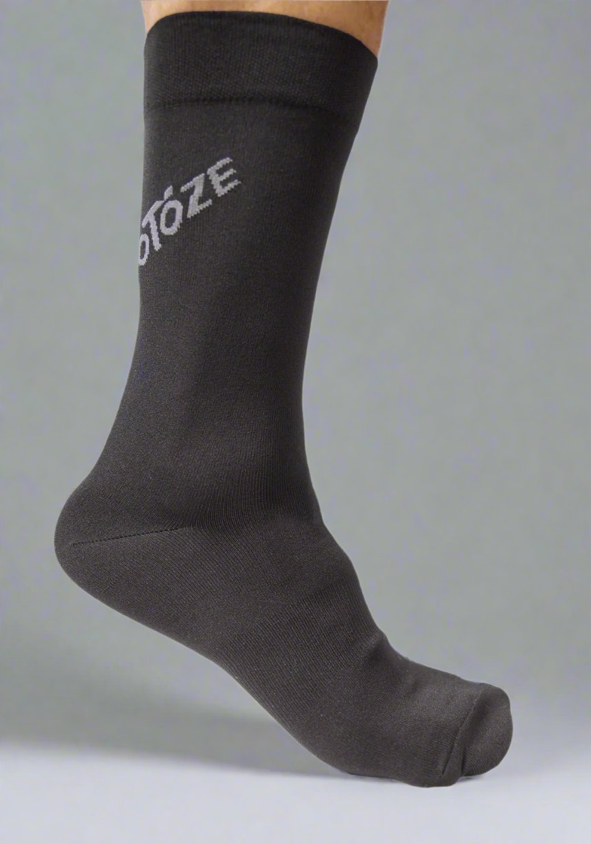 Black cycling sock with partial visible text, worn on foot, gray background