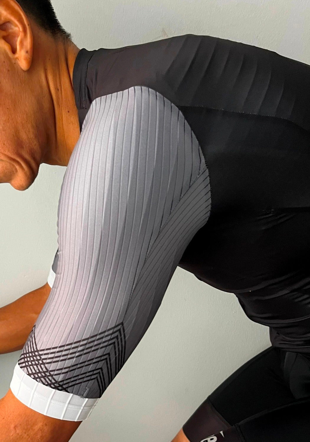 Cyclist wearing a black and gray ribbed short sleeve cycling jersey with geometric patterns