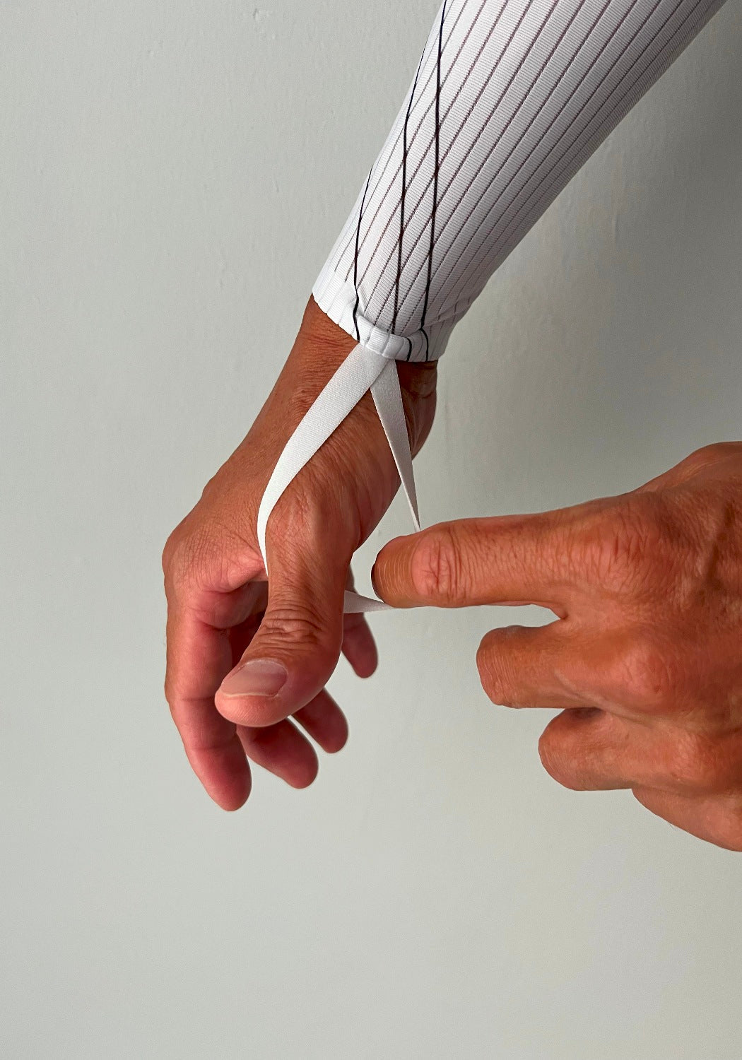 Cyclist's hand securing white, striped long-sleeve cycling jersey with thumb loop